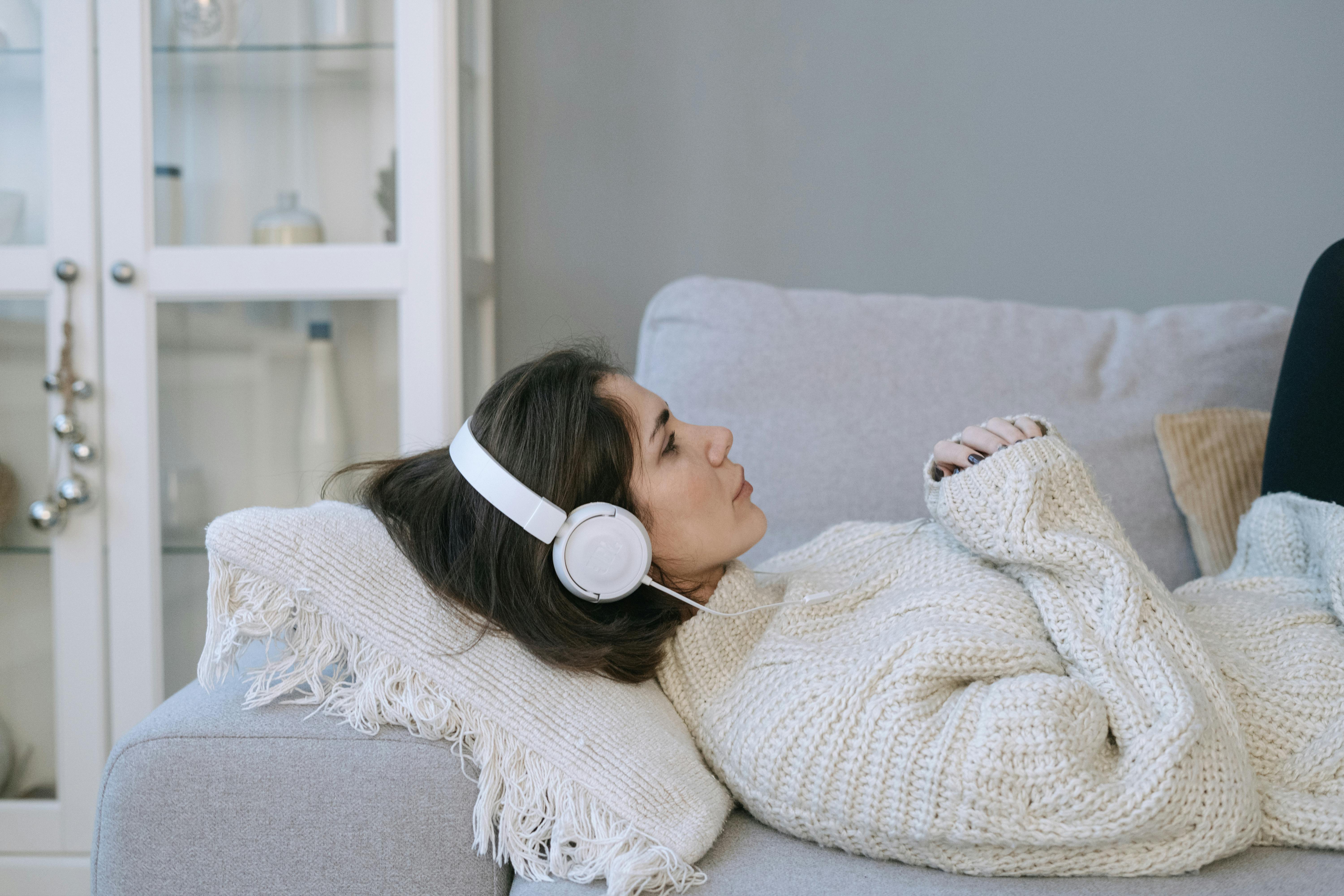 Sad woman laying down on a couch with headphones