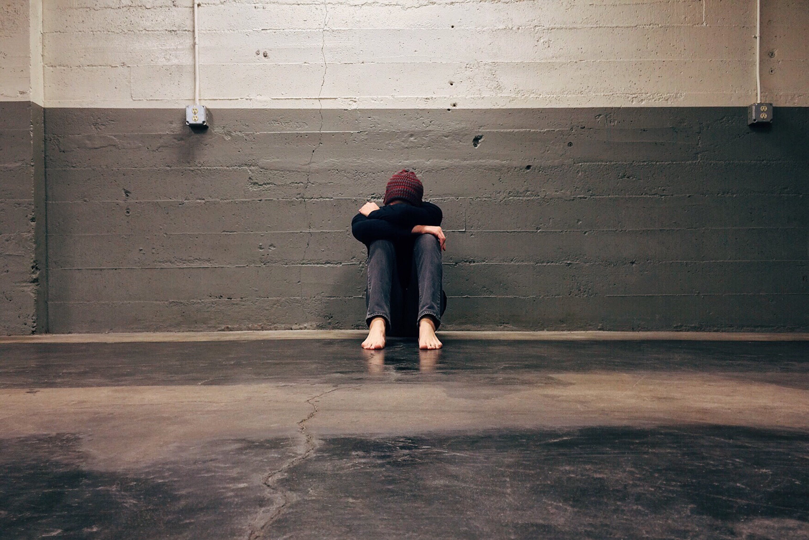 Person sitting alone by the wall with their head between their legs.